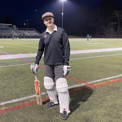 Cricket player wearing protective gear and holding a bat on a field at night.